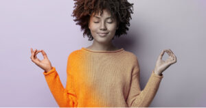 woman of color in an orange shirt meditating in front of a purple wall