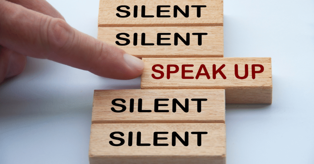 five wood blocks in a line, four of them say "silent", a finger pushes against the fifth, the one in the middle, which says "speak up"