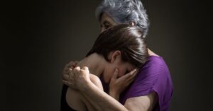 Older woman in purple shirt hugging younger woman ini black shirt who is crying.