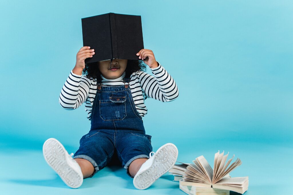 Young, shy child hiding behind a book.